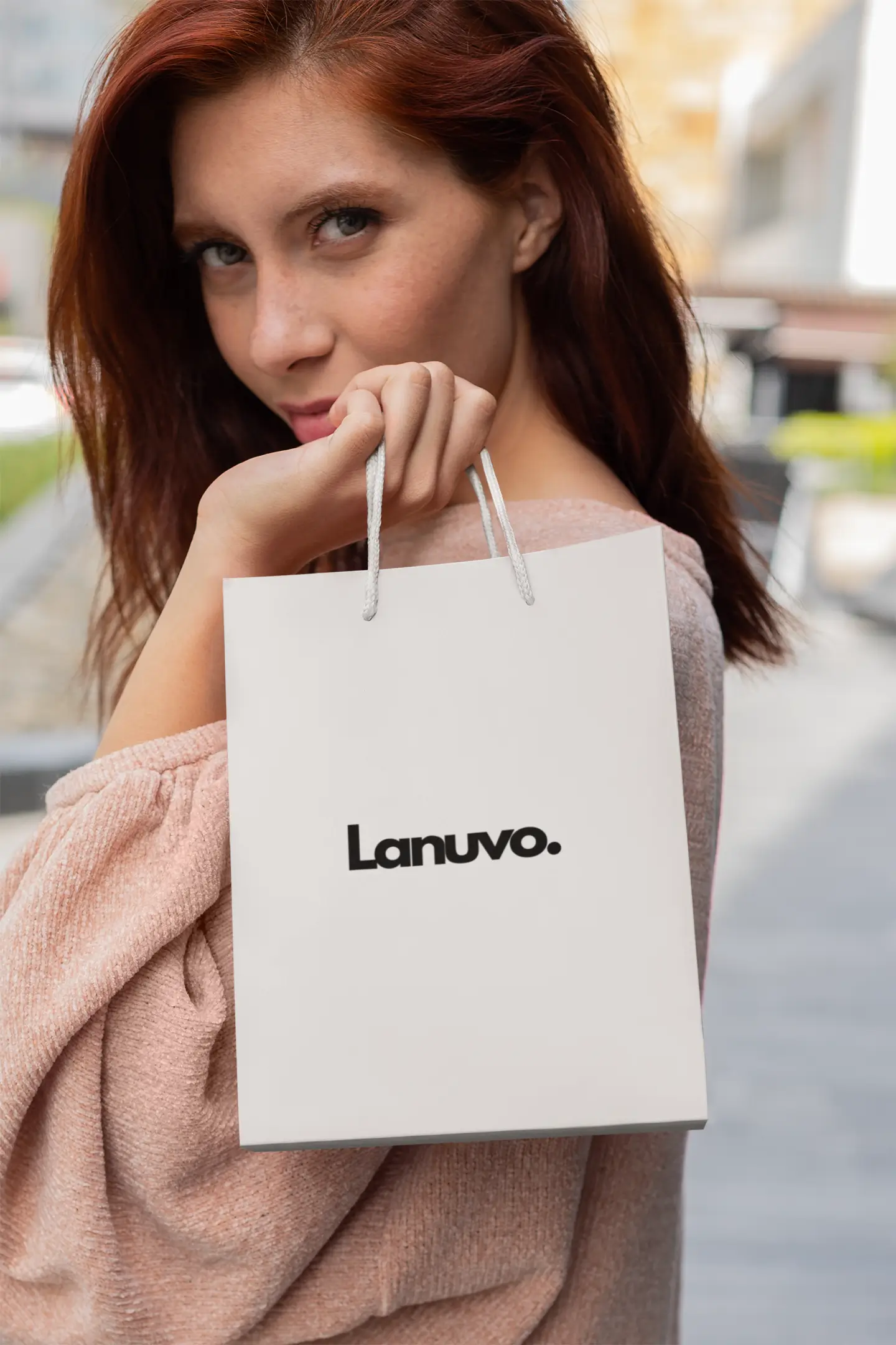 Woman holding a white shopping bag with 'Lanuvo' branding outdoors.